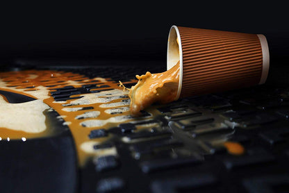 A cup of coffee mid-spill onto the floor of a car with a floor mat. 
